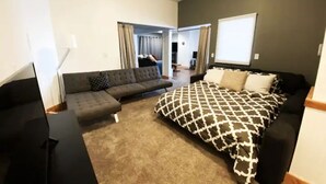 Ein Schlafzimmer mit Bett, Sofa und Schreibtisch. Ein Fenster und eine Tür zu einem anderen Raum.