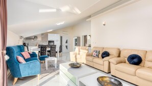 Un salón amplio con un sillón azul, sofá beige y una mesa de centro de cristal.