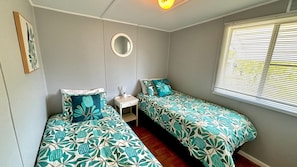 A room with two beds, a small table, a mirror, and a window with blinds.