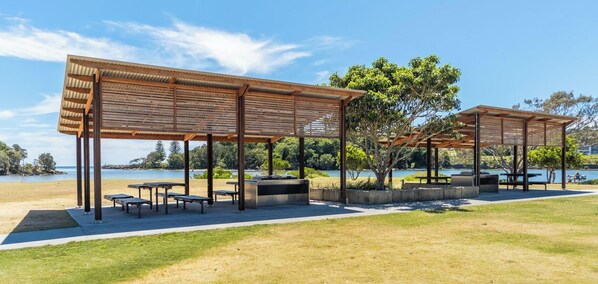 Deux aires de pique-nique abritées, équipées de tables et de bancs, un espace verdoyant au premier plan et une étendue d'eau en arrière-plan.