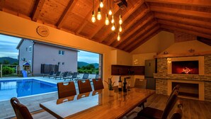 Un vaste espace dédié à la salle à manger, avec vue sur la piscine, une cheminée en pierre et un plafond en bois.