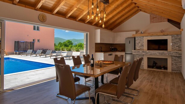 Une cuisine moderne avec un mur de crédence en pierre, un coin repas doté d’une table en verre, et une vue sur une piscine et des montagnes.