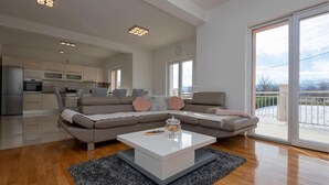 Un salon moderne avec un canapé d’angle, une table basse et une vue sur la cuisine et le balcon.