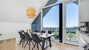 A modern dining area with a large table, black chairs, and a hanging light fixture. - 4 bedroom stunning home in Skagen (Skagen)