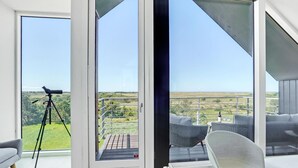 A modern room with a large sliding glass door leading to an outdoor balcony with a view of a grassy landscape. - 4 bedroom stunning home in Skagen (Skagen)