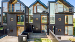 A modern multi-story house with large windows, balconies, and a wooden deck. - 4 bedroom stunning home in Skagen (Skagen)