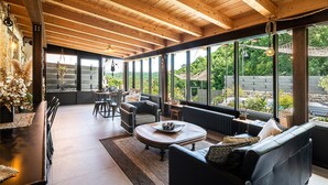 A spacious room with a high ceiling, large windows offering a view of the outdoors, a dining area with chairs and a table, and a cozy seating area with a sofa and a coffee table. - 3 bedroom awesome home in Filignano (Filignano)