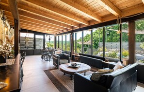 A spacious room with a high ceiling, large windows offering a view of the outdoors, a dining area with chairs and a table, and a cozy seating area with a sofa and a coffee table. - 3 bedroom awesome home in Filignano (Filignano)