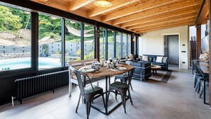 Un comedor amplio con una mesa grande y sillas, vista a una piscina, y un rincón de descanso acogedor con un sofá y una mesita de centro.