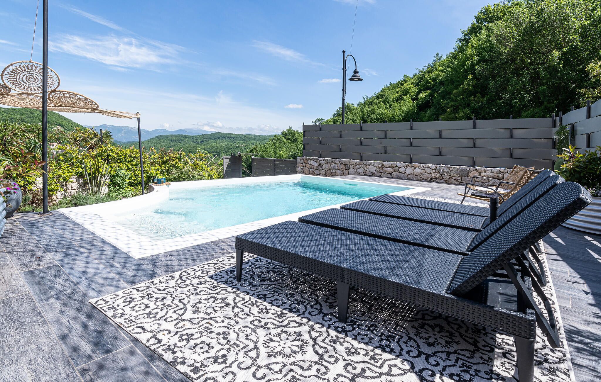 Una piscina en la azotea con sillones de descanso, un muro de piedra y vistas a montañas.