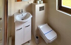 Une salle de bain avec un lavabo blanc, deux armoires, des toilettes et une fenêtre.