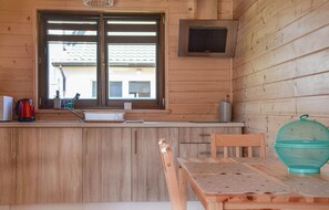 L’intérieur d’un chalet en bois comprend un coin cuisine équipé d’un évier, d’une bouilloire, d’un grille-pain, d’un four à micro-ondes et d’une fenêtre avec des stores.