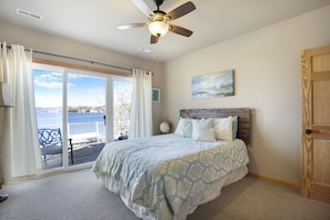 Une chambre avec un lit, un ventilateur de plafond, une vue sur l’eau et une porte.