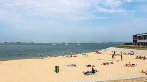 A beach with people sunbathing and swimming, a pier with a building, and sailboats on the water. - Beautiful home in Sint-Annaland (Sint-Annaland)