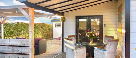 A covered patio with wicker chairs, a table, and a vase of flowers.