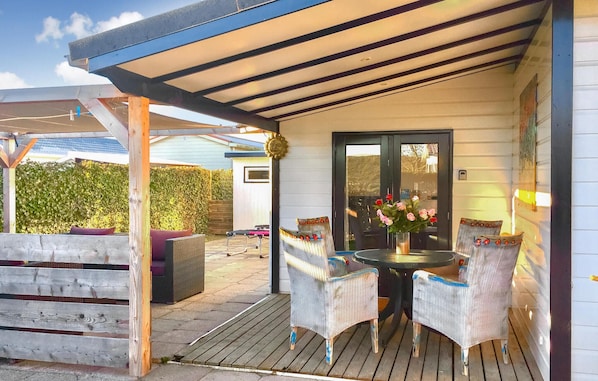Een overdekt terras met rieten stoelen, een tafel en een bloevas.