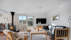 A cozy living room with a fireplace, a sofa, a coffee table, and a bookshelf. - 3 bedroom cozy home in Blokhus (Blokhus)