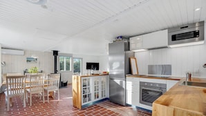 A modern kitchen with a brick floor, white cabinetry, stainless steel appliances, and a dining area with wooden chairs. - 3 bedroom cozy home in Blokhus (Blokhus)