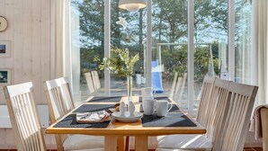 A dining area with a wooden table, white chairs, and a vase with greenery. - 3 bedroom cozy home in Blokhus (Blokhus)