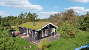 A cabin with a green roof, a deck, and a small outdoor seating area. - 3 bedroom cozy home in Blokhus (Blokhus)