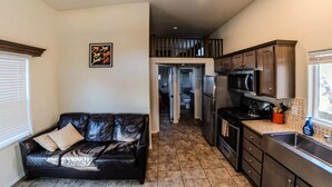 A compact living space with a kitchenette, a black leather sofa, and a framed artwork on the wall.