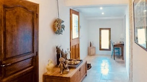 Un couloir avec une porte en bois, une petite table ornée d’objets décoratifs, un miroir et une fenêtre laissant entrer la lumière naturelle.