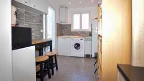 A compact kitchen with a washing machine, a small dining area with stools, and a window providing natural light.