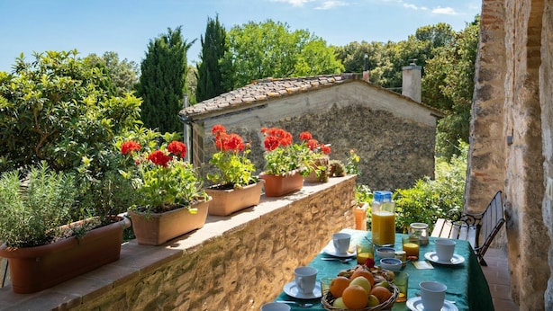 Terraço com plantas em vasos, mesa posta para o café da manhã e um edifício de pedra ao fundo.