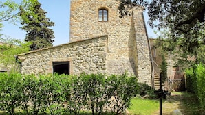 Um edifício de pedra com uma pequena janela e uma porta aberta, rodeado por vegetação.