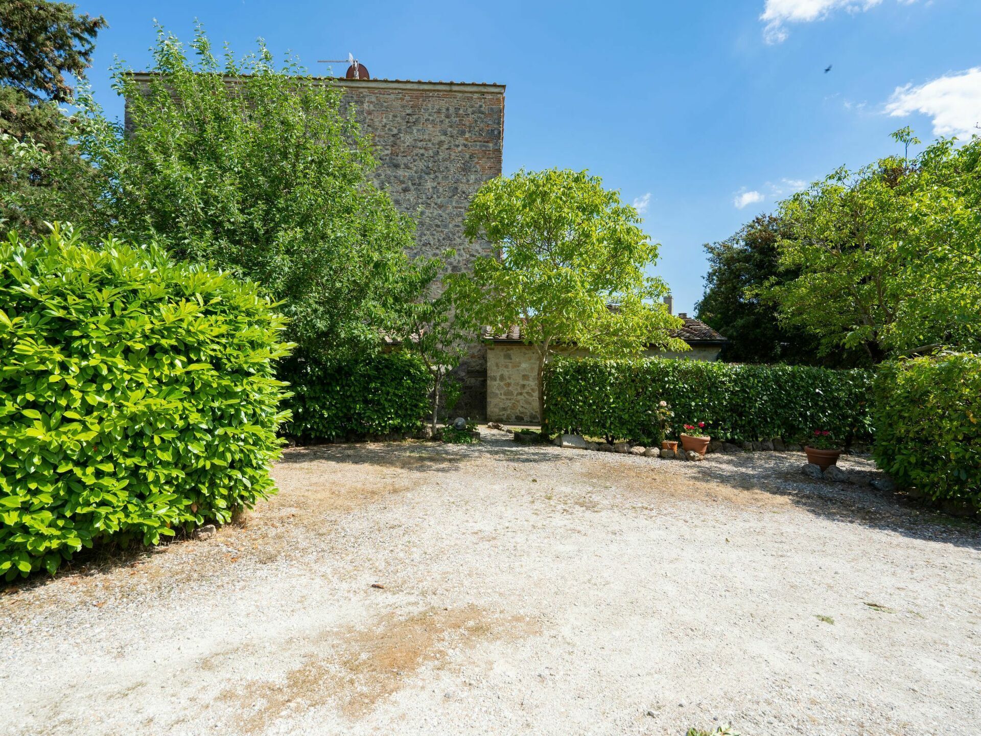 A courtyard with a stone wall, gravel ground, and various green shrubs.