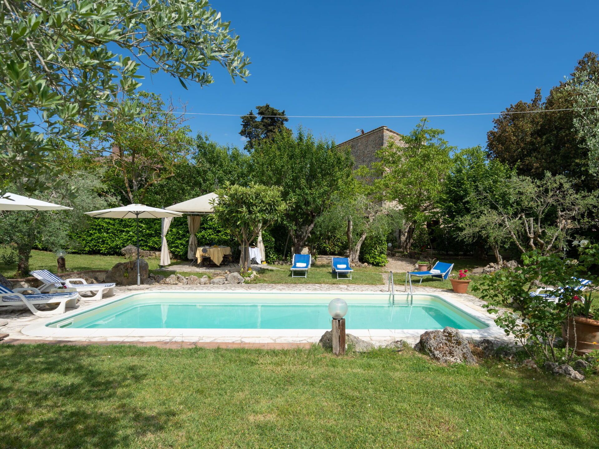 A backyard with a swimming pool, lounge chairs, and a covered patio area.