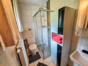 Bathroom features a glass-enclosed shower, toilet, sink, and shelf.