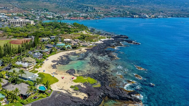 Une zone côtière comprenant une plage, une côte rocheuse et une vue sur une ville en arrière-plan.