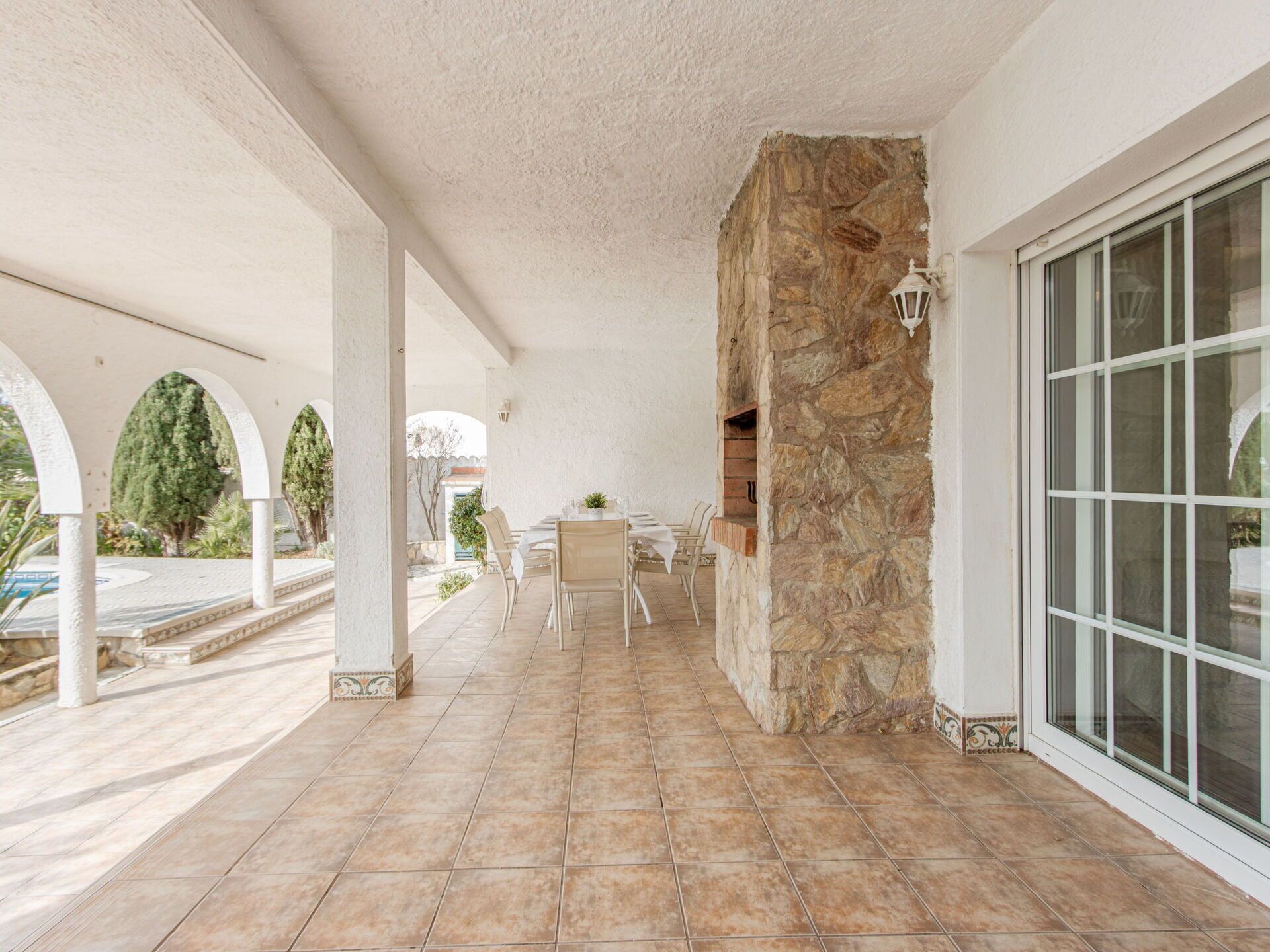 A covered patio area with a stone wall, a table with chairs, and a view of the outdoors.