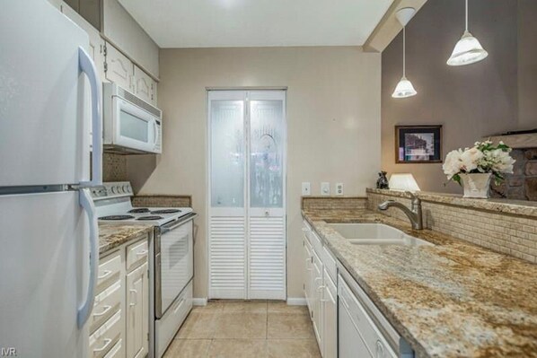Una cocina moderna con electrodomésticos blancos, encimeras de granito, un lavabo doble y una puerta de vidrio esmerilado.