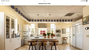 Una cocina moderna con armarios blancos, una isla central con taburetes y platos decorativos azules en la pared.