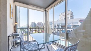 Ein moderner Balkon mit einem Glastisch und weißen Stühlen, der einen Blick auf die Stadtarchitektur bietet.
