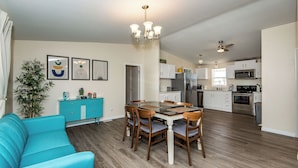 A modern kitchen with white cabinets, stainless steel appliances, and a dining area with a blue sofa and wooden chairs. - Quiet Oasis Near the Colorado River STR (Bullhead City)