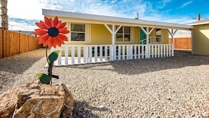 A house with a white porch, a large flower decoration, and a gravel driveway. - Quiet Oasis Near the Colorado River STR (Bullhead City)