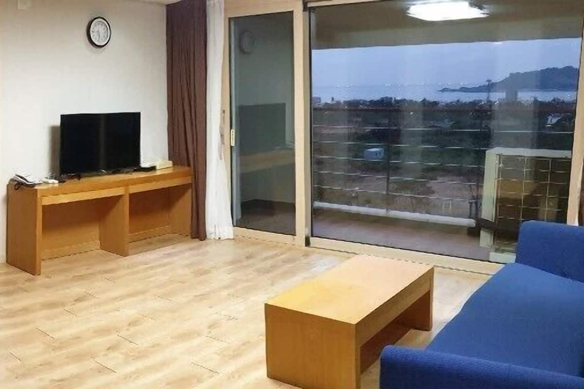 Un salon avec un canapé, un téléviseur posé sur un meuble en bois et un balcon avec vue.