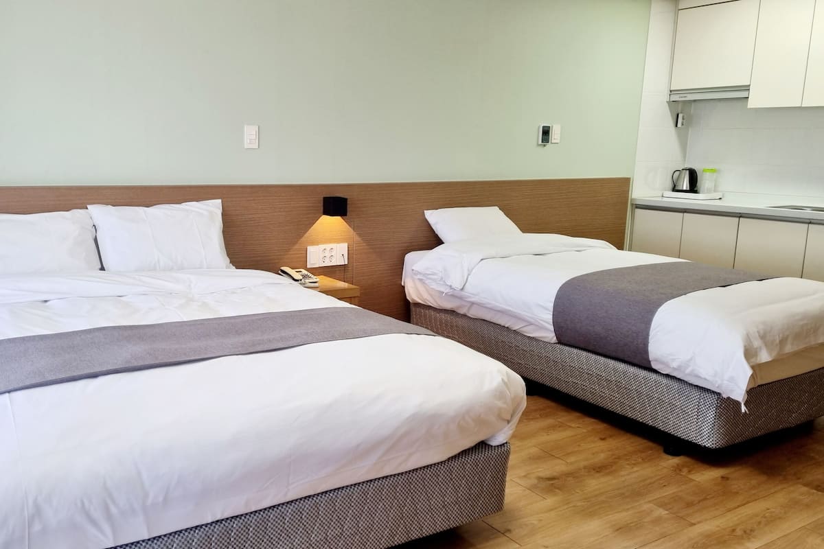Deux lits avec du linge de lit blanc, une table de chevet avec une lampe, un téléphone et une prise électrique murale.