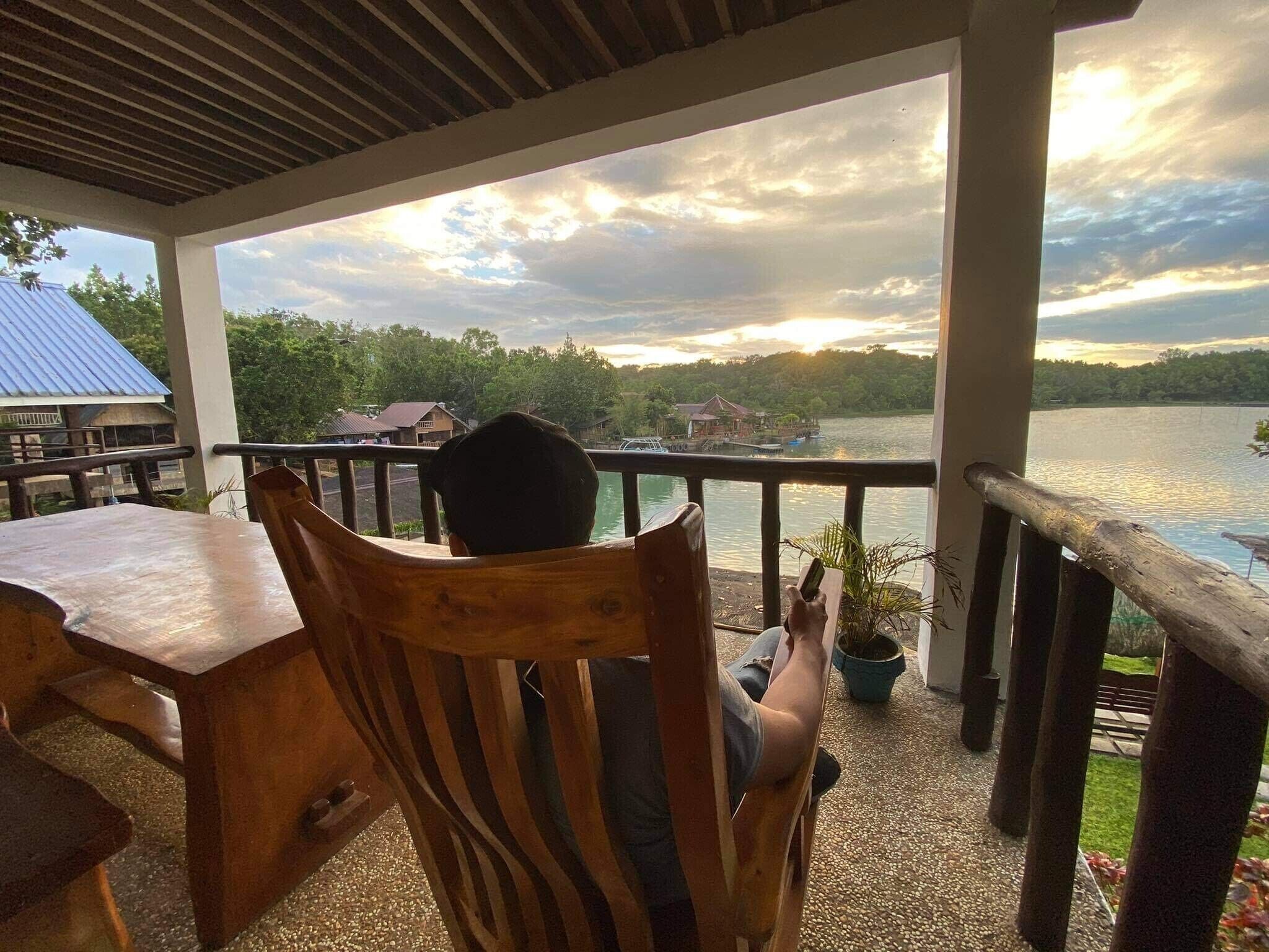 Una silla de madera orientada hacia una vista del lago, con una mesa de madera a su lado.