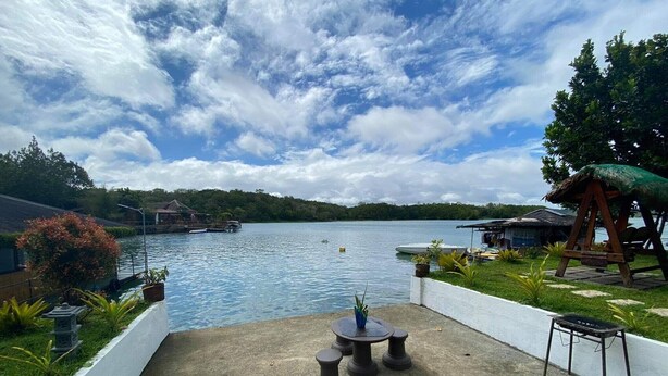 Un patio frente al agua con una mesa y sillas, con vista a un lago con barcos y casas al fondo.