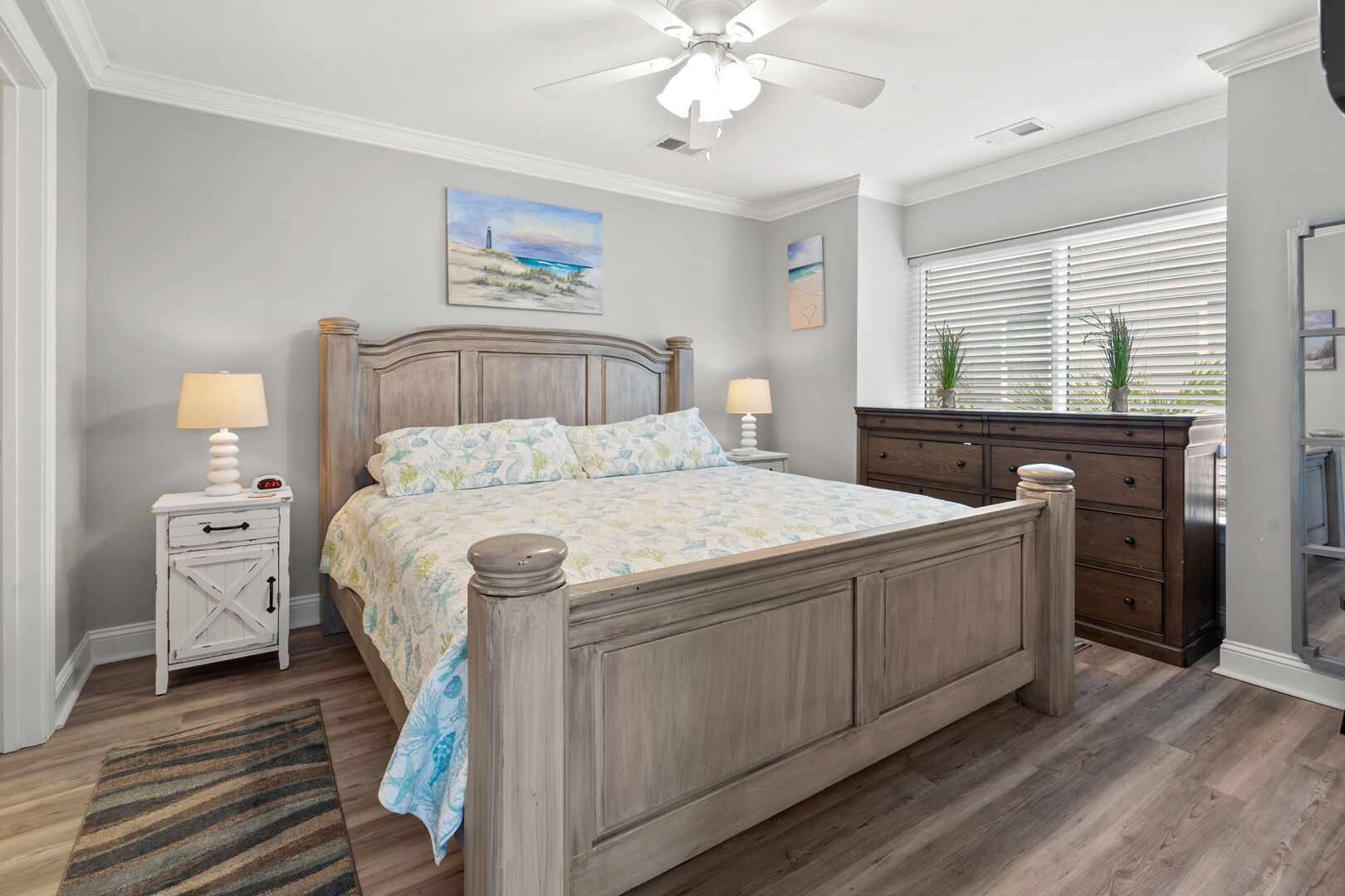 Une chambre à coucher avec un lit en bois, deux tables de chevet avec des lampes, une commode et une fenêtre avec des stores.
