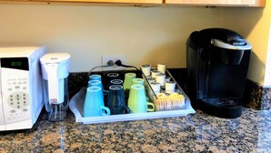 A kitchen with a microwave, coffee maker, and a tray of mugs.