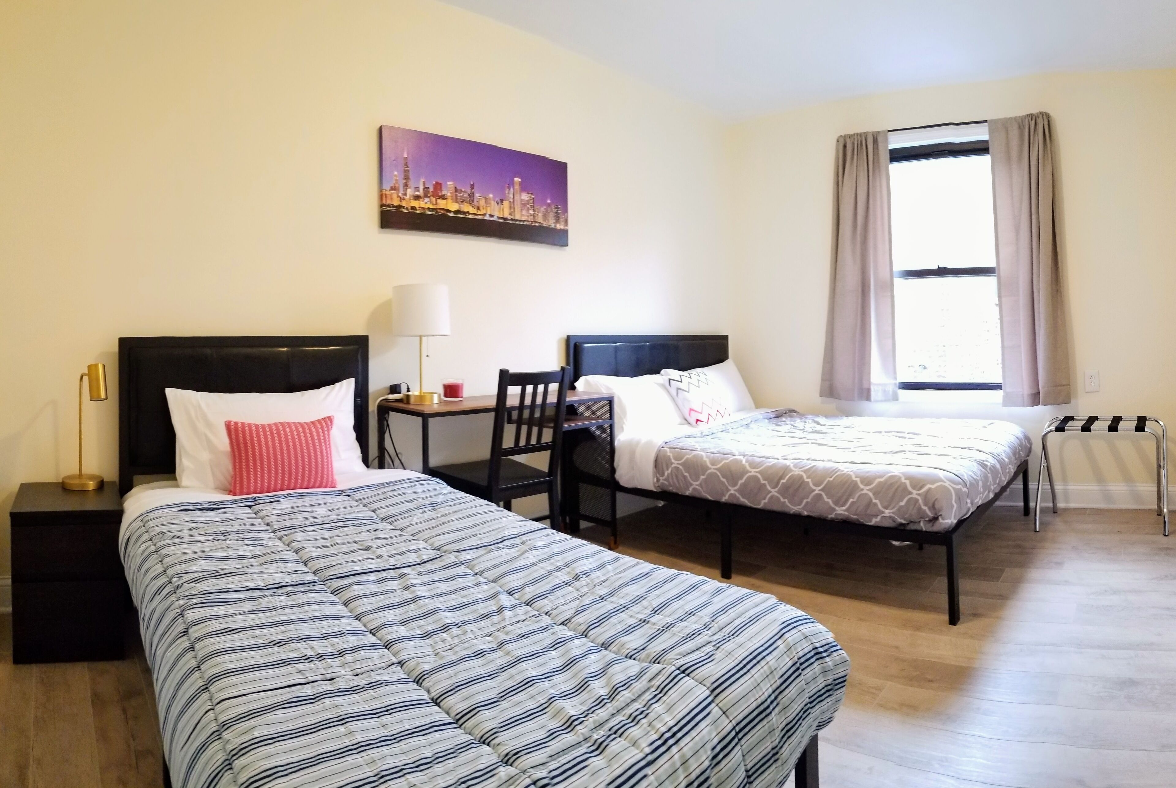 A hotel room with two beds, a desk, a chair, a lamp, and a window with curtains.