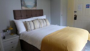 Una cama bien tendida con un almohadón a rayas y un edredón amarillo, una lámpara de noche y una mesita de noche con cajones.
