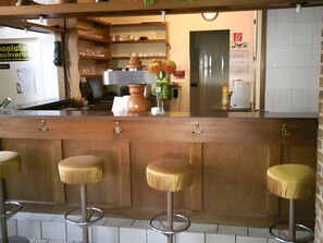 A bar area with stools, a counter, and a vase with flowers. - Hotel Burghof (Stolberg)