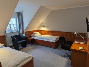 A hotel room with a sloped ceiling, a bed, a desk with a lamp, two chairs, and a window with curtains. - Historik Hotel Garni Christinenhof (Hamelin)