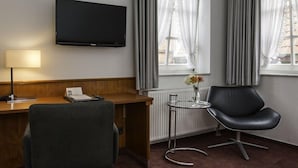 Une chambre d’hôtel équipée d’un bureau, d’une chaise, d’une télévision et d’une fenêtre avec des rideaux.